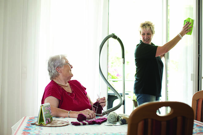 Jüngere Frau putzt Fenster, eine älter Dame schaut lächelnd zu