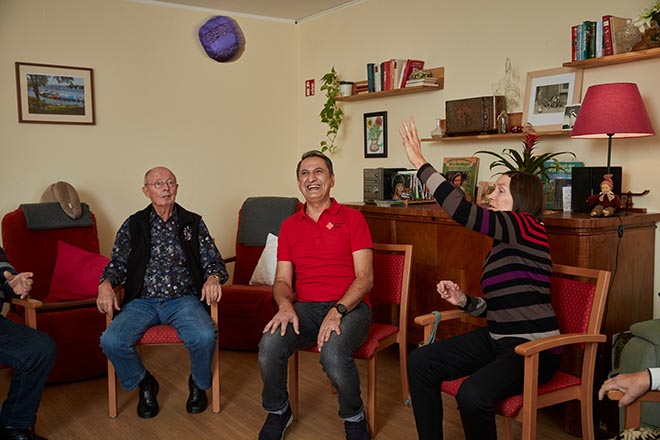 DRK-Mitarbeiter sitzt zwischen zwei Senioren, die sich einen Ball zu werfen