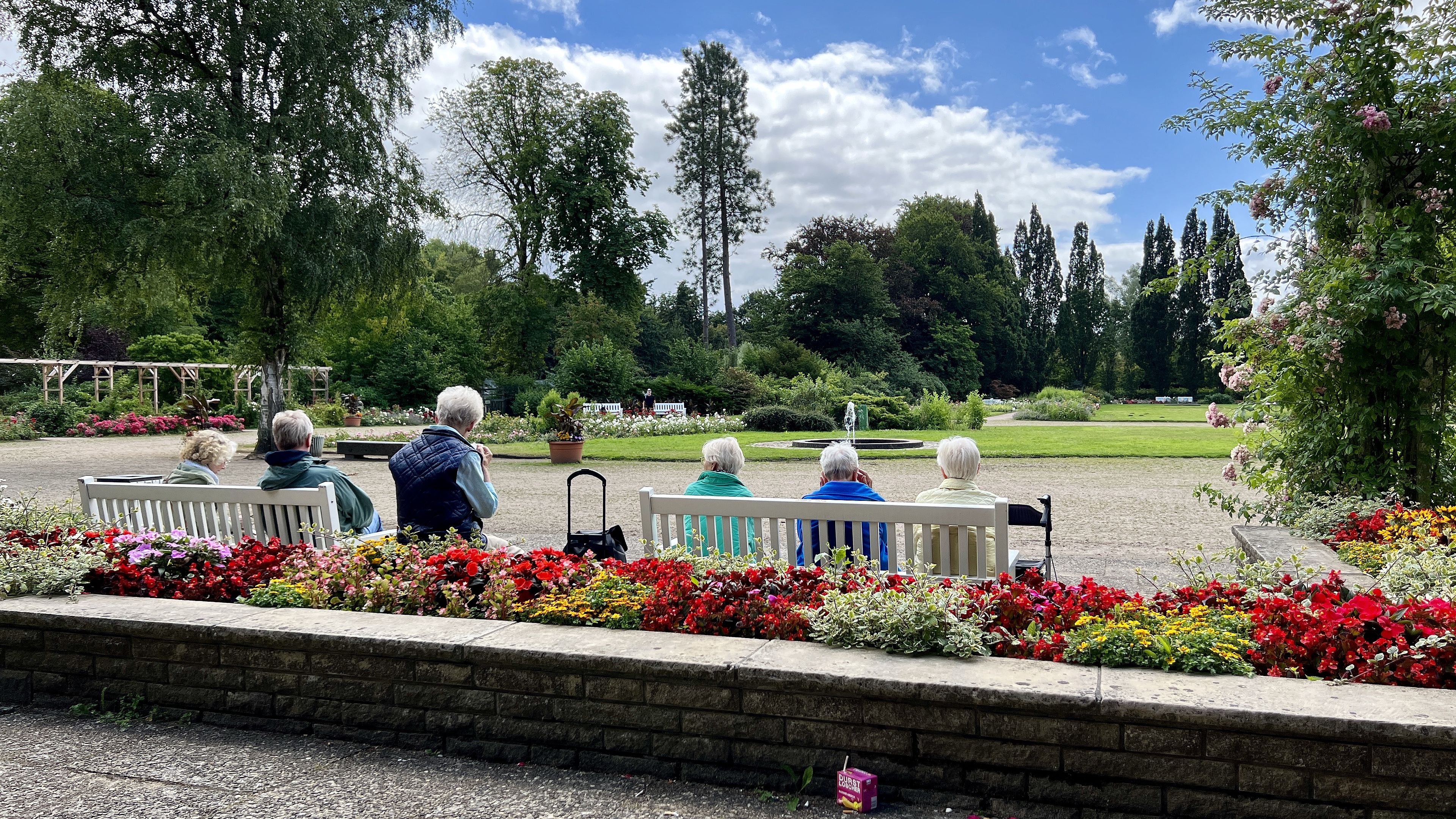 Vier Gäste der Tagespflege sitzen auf einer Parkbank und schauen ins Grüne