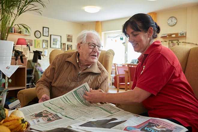 DRK-Mitarbeiterin und ein Senior blättern gemeinsam in der Zeitung