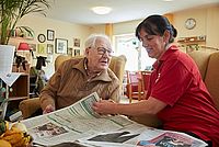 DRKlerin und Senior lesen gemeinsam die Tageszeitung