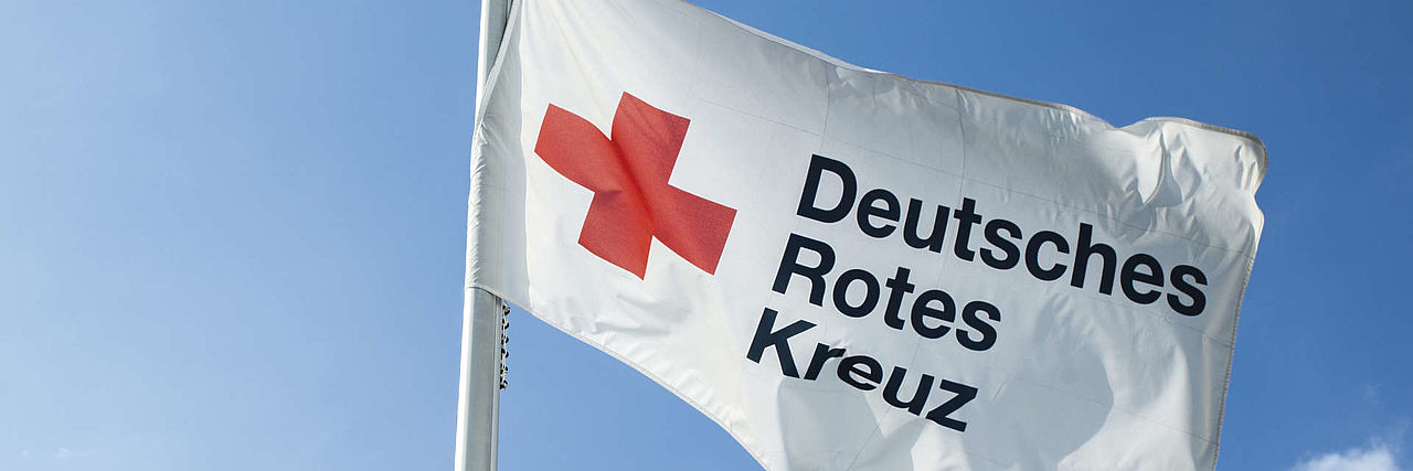 Fahne mit DRK-Logo und Schriftzug vor blauem Himmel