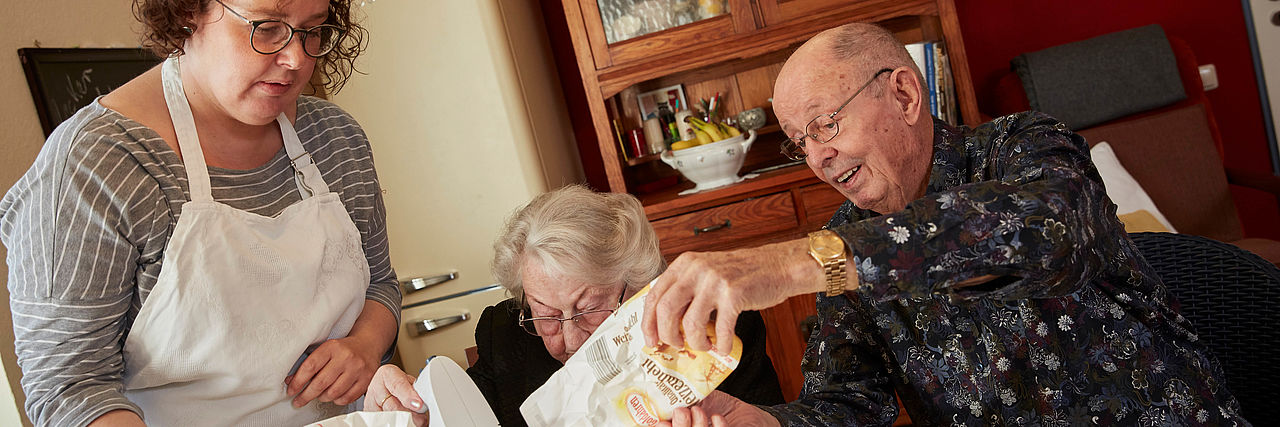 DRKlerin hilft einem Senioren-Paar beim Backen