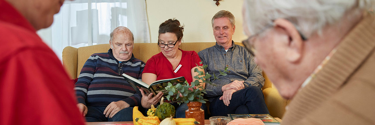 DRKlerin sitzt zwischen zwei Senioren auf dem Sofa